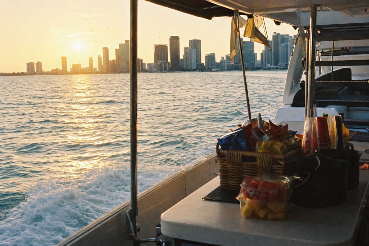 A yacht cruising Biscayne Bay at sunset with the Miami skyline glowing behind it, no text, no logos, no people