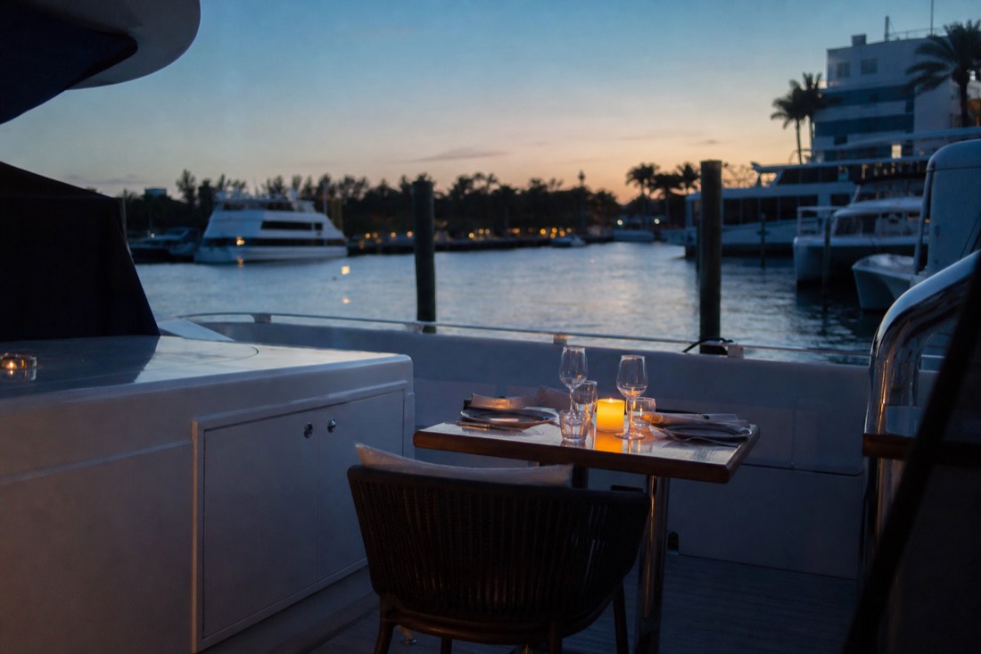 A dinner table set on the deck of a yacht with the Miami skyline glowing at dusk in the background, no text, no logos, no people