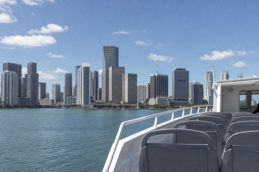 A child leaning on a boat railing pointing at the Downtown Miami skyline across Biscayne Bay, no text, no logos, no people