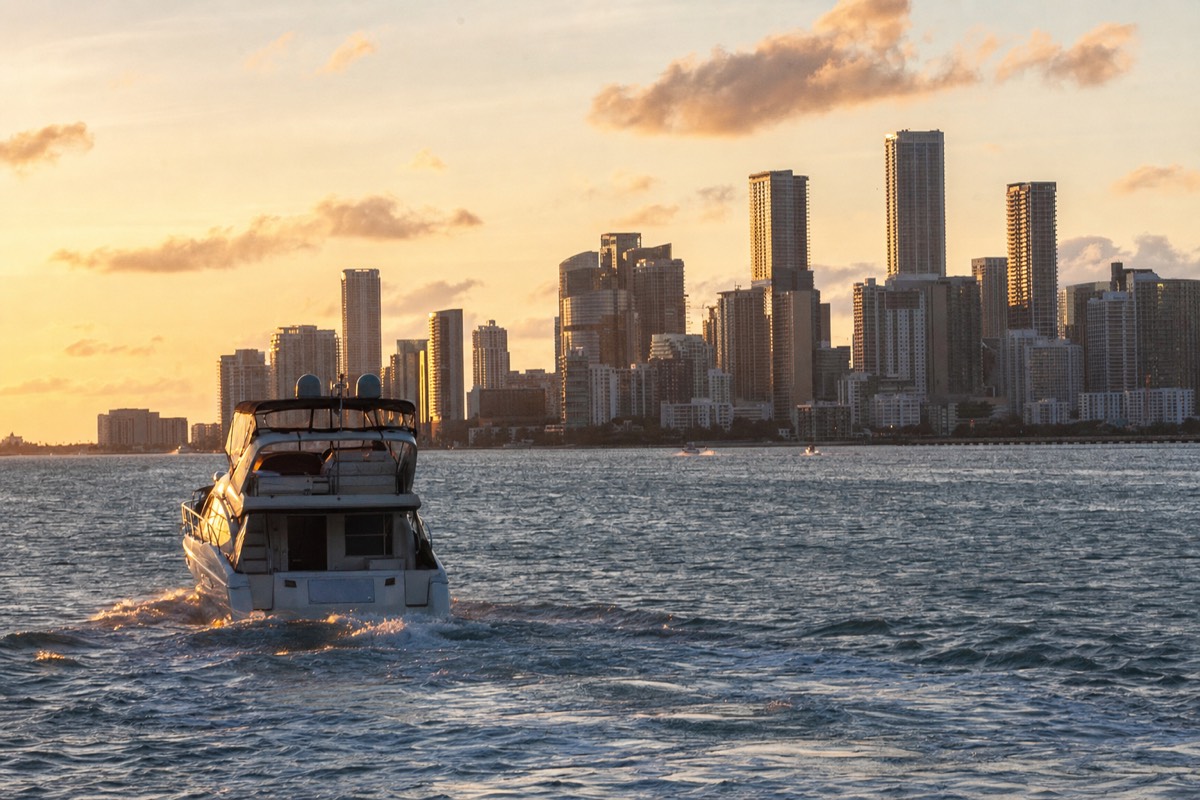 A boat cruising on Biscayne Bay at sunset with the Miami skyline glowing in the background, no text, no logos, no people