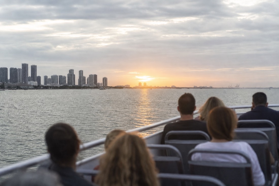 Passengers on an open upper deck watching the sun set over Biscayne Bay, no text, no logos, no people