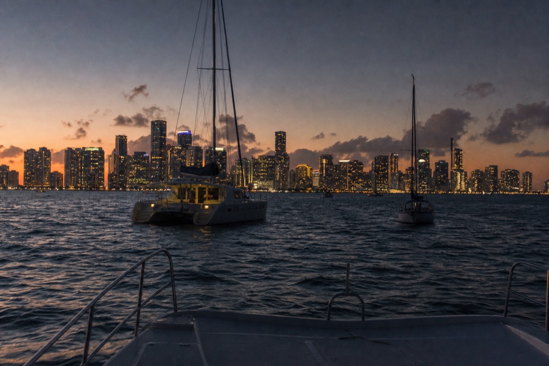 A catamaran and sailboat anchored near the Miami skyline at golden hour, no text, no logos, no people