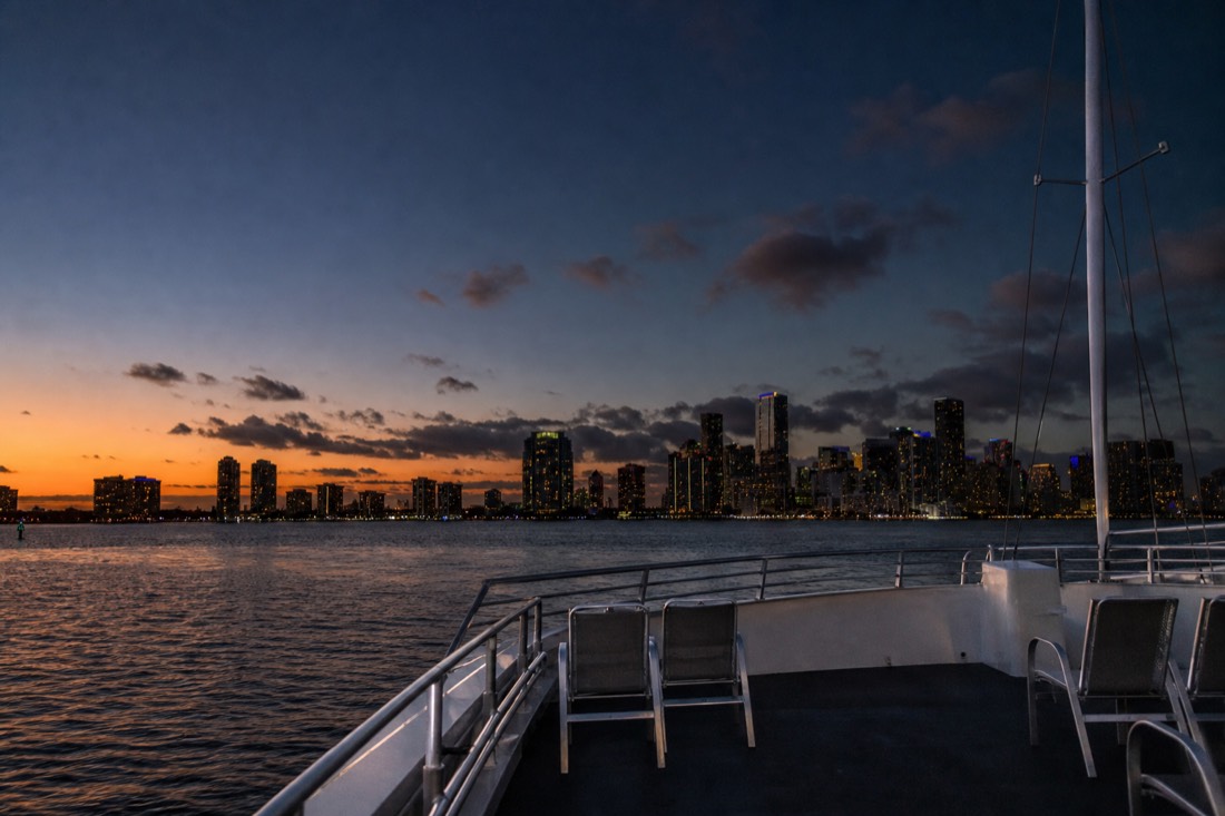 Open upper deck of a cruise boat at golden hour with Miami skyline behind, no text, no logos, no people.