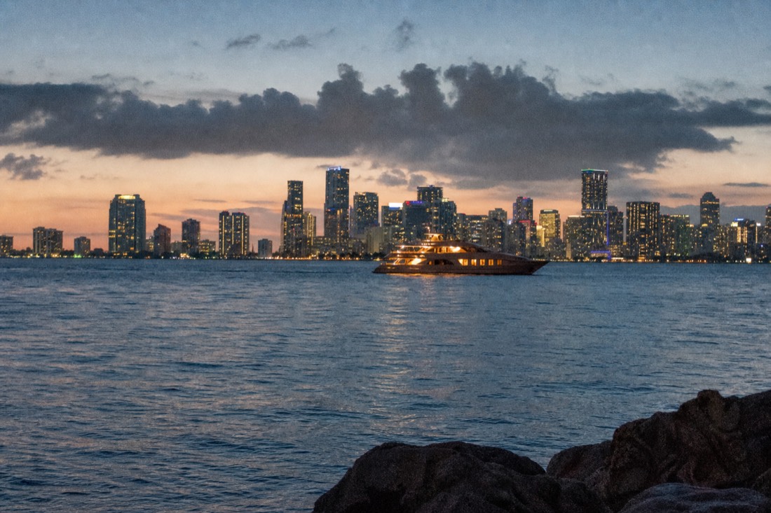 A cruise boat on Biscayne Bay with the illuminated downtown Miami skyline behind it at night, no text, no logos, no people.