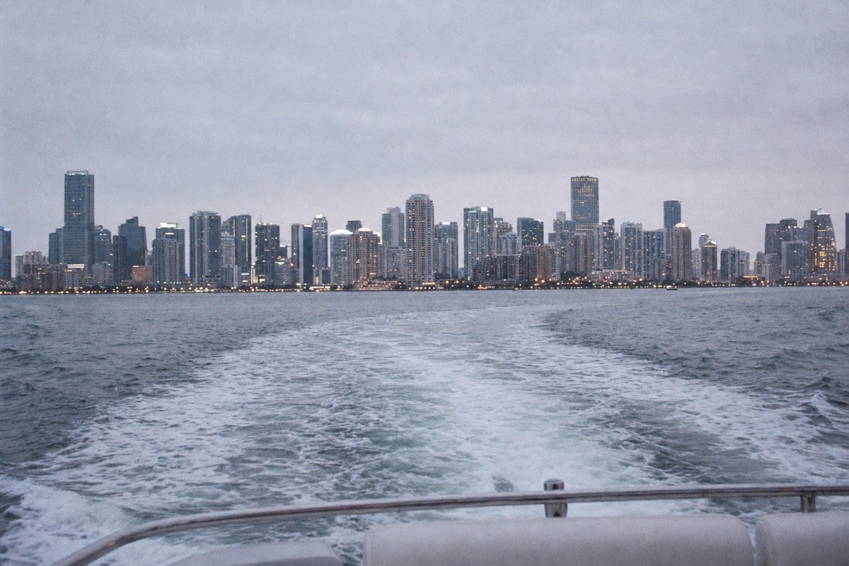 A boat cruising past Miami's downtown skyline at dusk across Biscayne Bay, no text, no logos, no people.