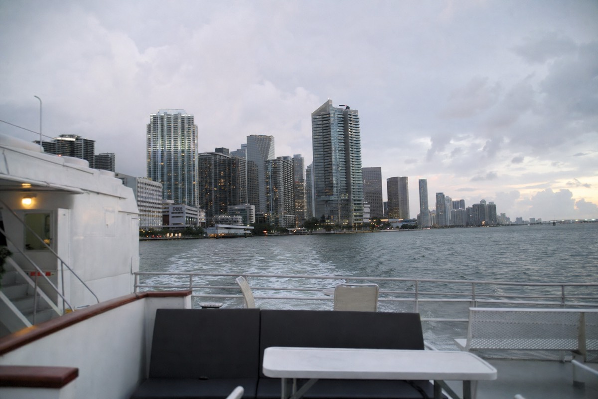 A double-deck sightseeing yacht cruising past the downtown Miami skyline at dusk, no text, no logos, no people