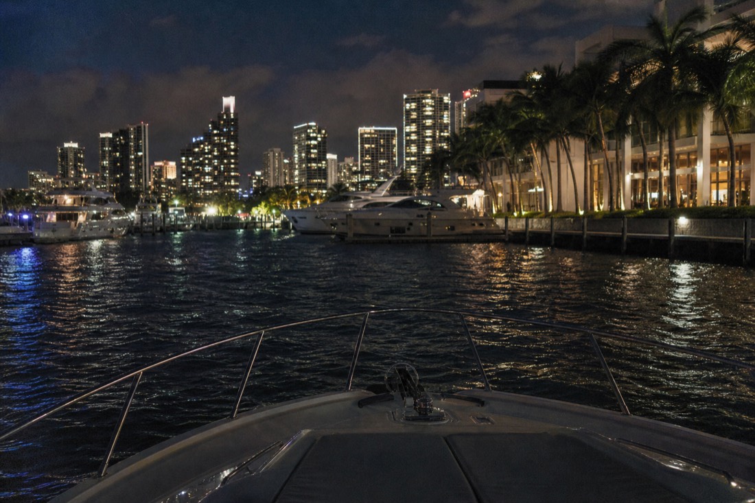 Passenger yachts docked at a marina beside a waterfront shopping complex at night, no text, no logos, no people