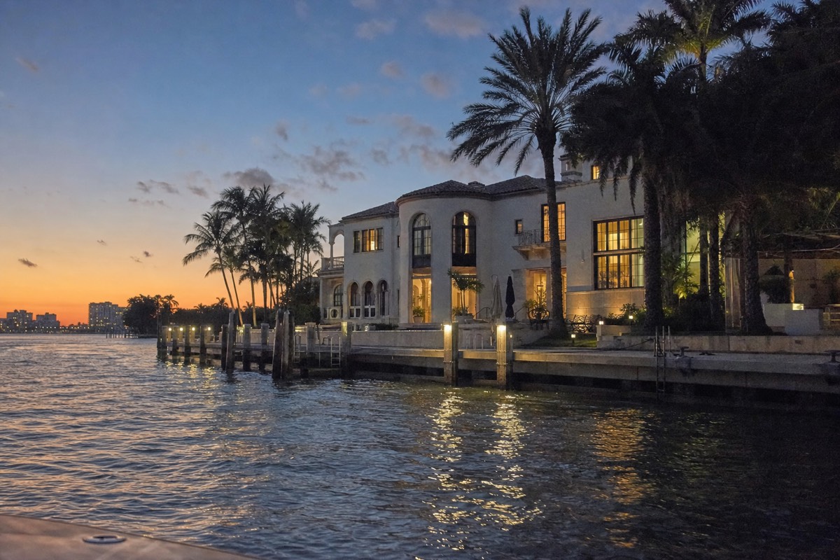 A luxury waterfront mansion on Star Island seen from the water at golden hour, no text, no logos, no people