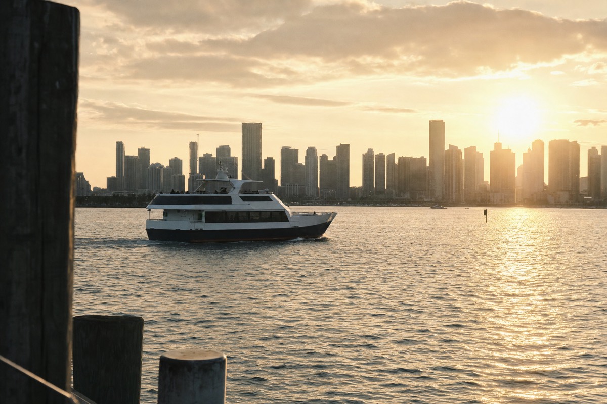 A passenger boat gliding across Biscayne Bay at sunset with the Miami skyline behind it, no text, no logos, no people.