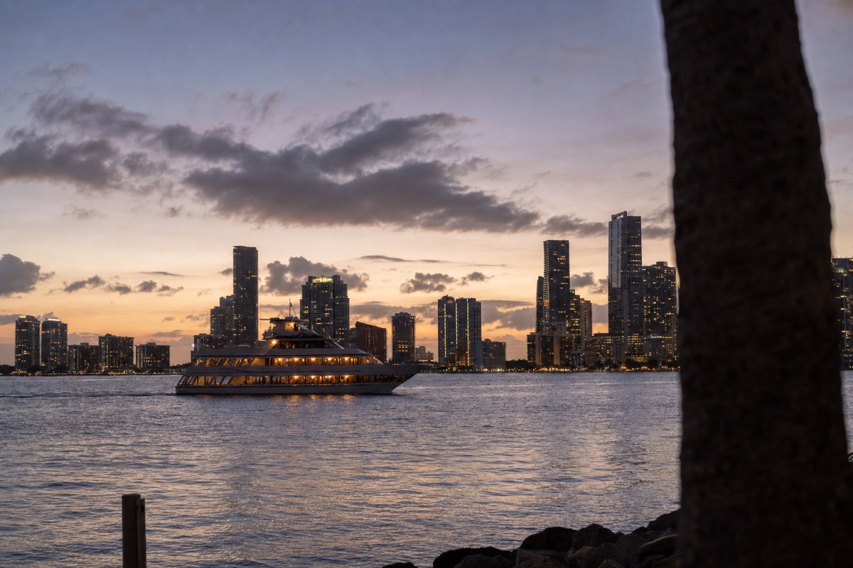 A Miami cruise boat on Biscayne Bay at dusk with the downtown skyline lit up behind it, no text, no logos, no people.