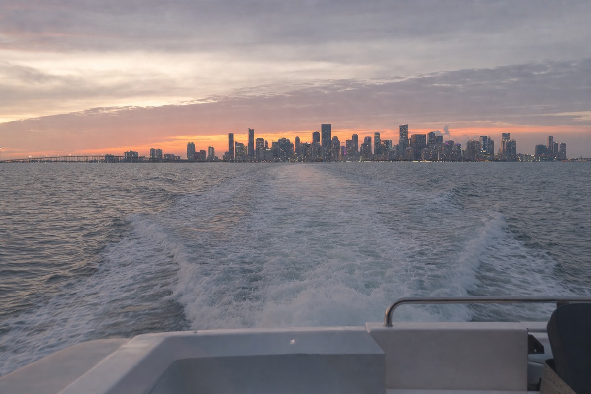 A boat crossing Biscayne Bay at sunset with the Miami skyline glowing in the background, no text, no logos, no people.