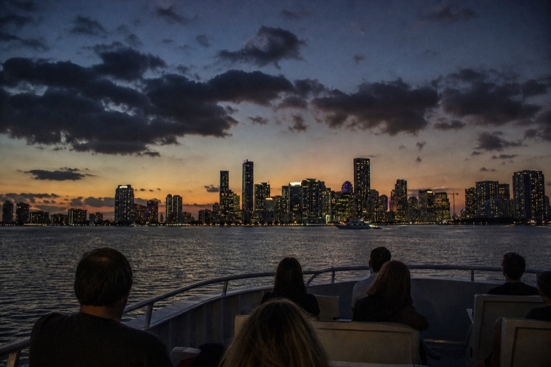 Passengers on an open upper deck watching the sun go down over Biscayne Bay, no text, no logos, no people.