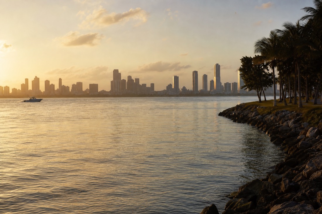 Golden sunset light over calm Biscayne Bay water with the Miami Beach skyline in the distance, no text, no logos, no people.